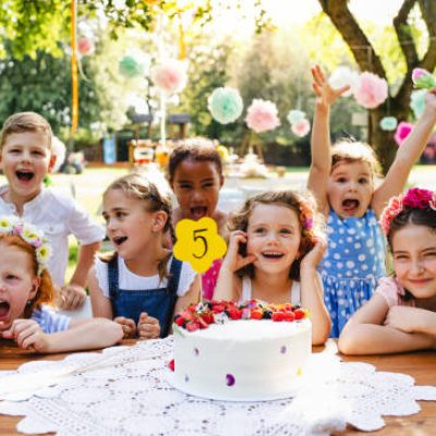 A portrait of children with cake standing around table on birthday party in garden in summer.